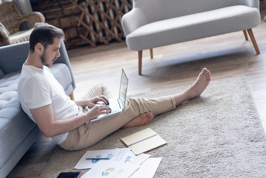 Muž pracující na notebooku sedí na podlaze se svým deníkem a oficiálními papíry doma - Fotografie, Obrázek