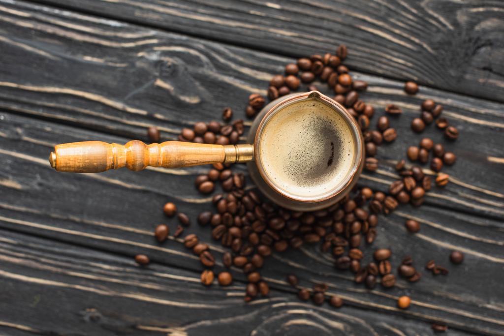 vrchní pohled na cezve s kávou na kávových zrnech na dřevěném povrchu - Fotografie, Obrázek