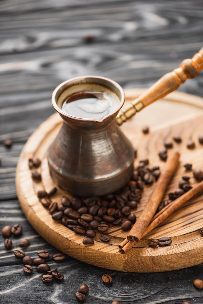selektywne skupienie cezve z kawą w pobliżu kijów cynamonowych na drewnianej desce - Zdjęcie, obraz
