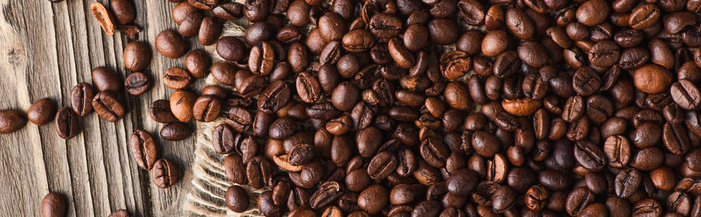 Draufsicht auf Kaffeebohnen verstreut auf Holzoberfläche, Panoramaaufnahme - Foto, Bild
