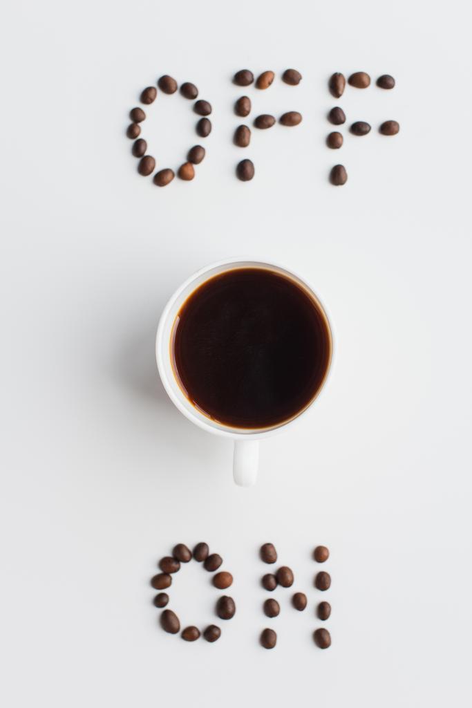 白い表面のカップの近くにコーヒー豆で作られたレタリングの上と下のビュー - 写真・画像