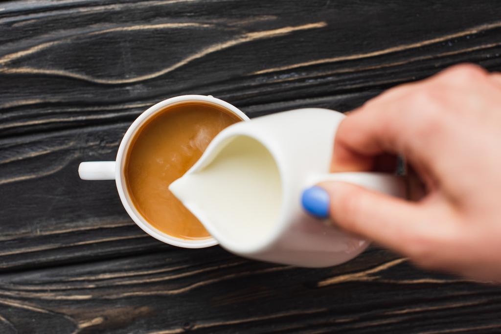 oříznutý pohled baristy přidávající mléko do kávy v šálku na dřevěném povrchu - Fotografie, Obrázek