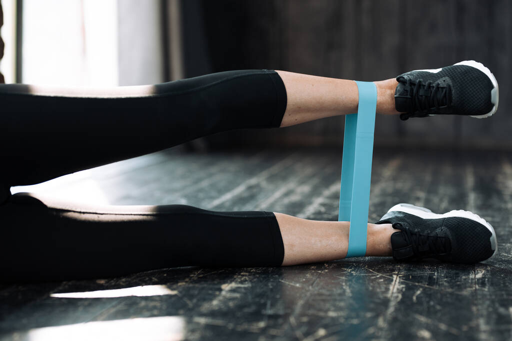 Zbliżenie kobiecej nogi ze sportowym elastycznym paskiem do treningu. Dziewczyna fitness trener robi ćwiczenia dla nóg - Zdjęcie, obraz