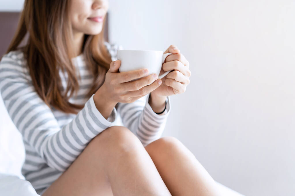 Молода жінка розслабляється в затишній домашній атмосфері і дивиться вікно на ліжко з чашкою кави вранці
 - Фото, зображення