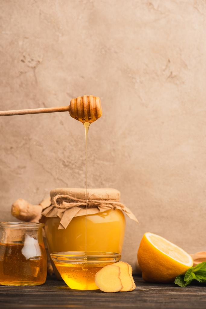 sladký med, mátové listy, zázvorový kořen a citron na dřevěném povrchu v blízkosti béžové betonové stěny - Fotografie, Obrázek