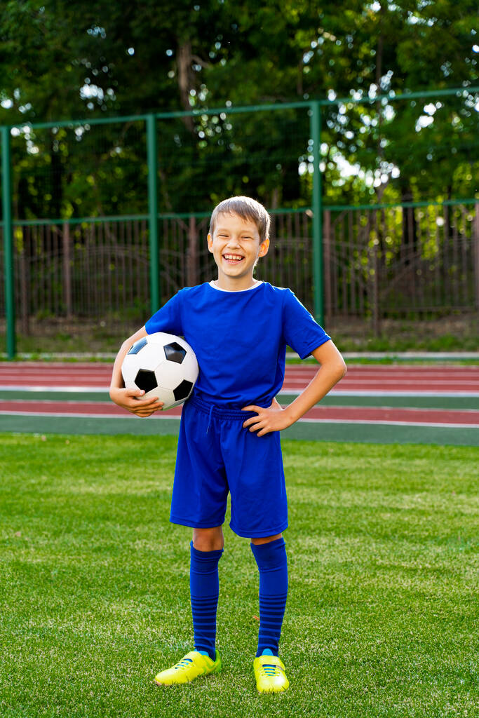 un piccolo giocatore di calcio con una palla si trova su un campo da calcio verde. - Foto, immagini