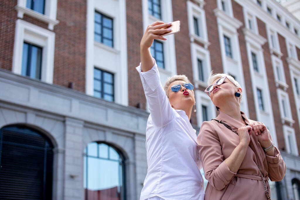stylowe dorosłych biznes kobiety pozować dla selfie poza w pobliżu biurowca - Zdjęcie, obraz