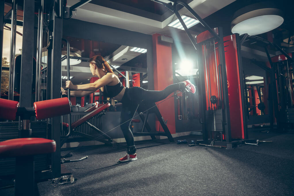 Jeune femme caucasienne musculaire pratiquant dans la salle de gym avec de l'équipement. Bien-être, mode de vie sain, musculation. - Photo, image