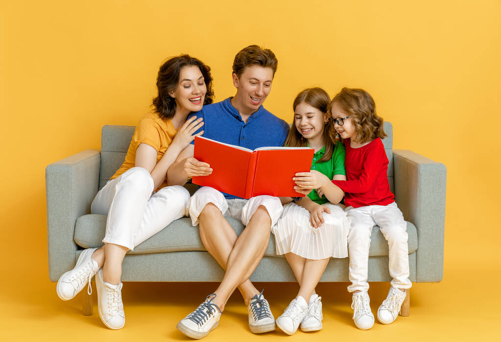Joyeux famille aimante. Mère, père et enfants filles lisant un livre sur fond jaune.  - Photo, image