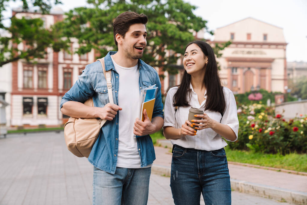 Kuva iloinen monikulttuurinen opiskelija pari puhuu ja juo kahvia takeaway kävellessään bulevardilla - Valokuva, kuva