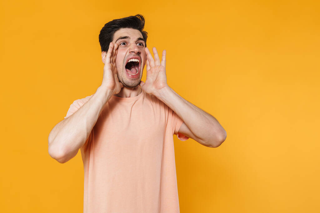 Fotografie zuřivého pohledný muž křičí s zvracením ruce izolované přes žluté pozadí - Fotografie, Obrázek