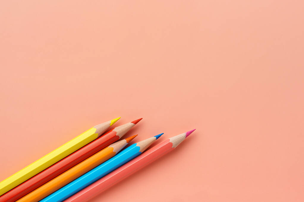 Buntstifte auf rosa Pastellgrund, flach gelegt. Unebene Reihe von Regenbogenstiften, Kopierraum. Bleistifte liegen diagonal in der linken unteren Ecke. - Foto, Bild