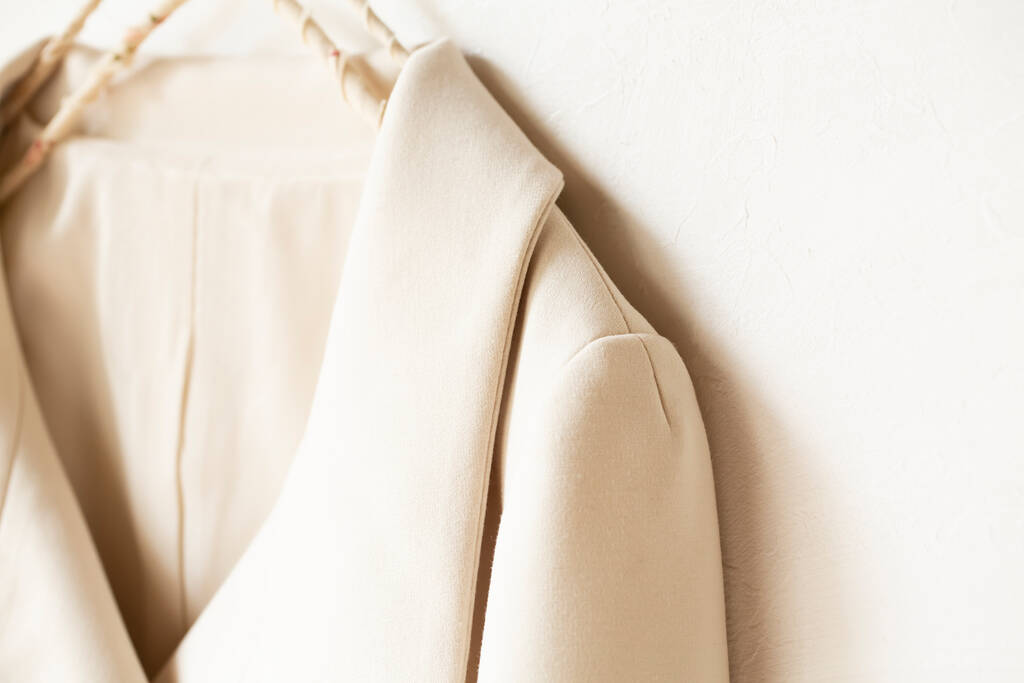 beige of witte jas hangend aan kleerhanger op witte achtergrond.close up. - Foto, afbeelding