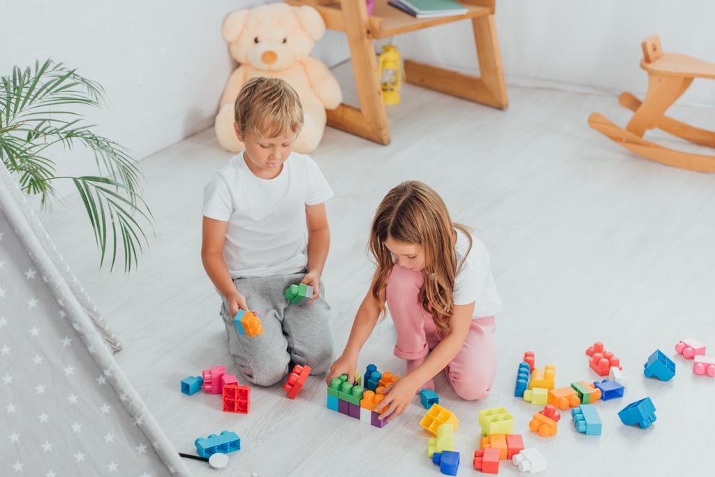 high angle view of children playing with building blocks while sitting on floor in pajamas - Photo, Image
