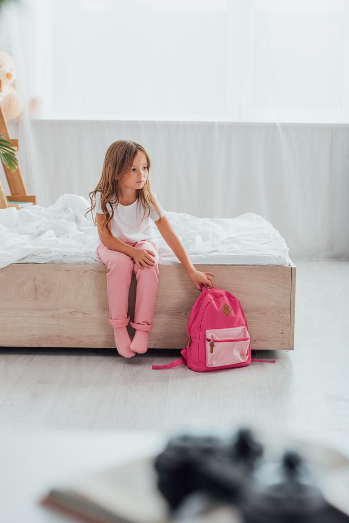 selective focus of girl in pajamas touching school backpack while sitting on floor in pajamas - Photo, Image