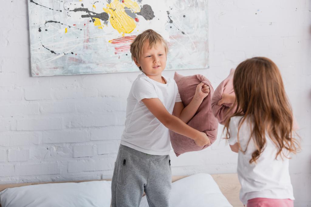 siblings in pajamas having fun while fighting with pillow in bedrooms - Photo, Image