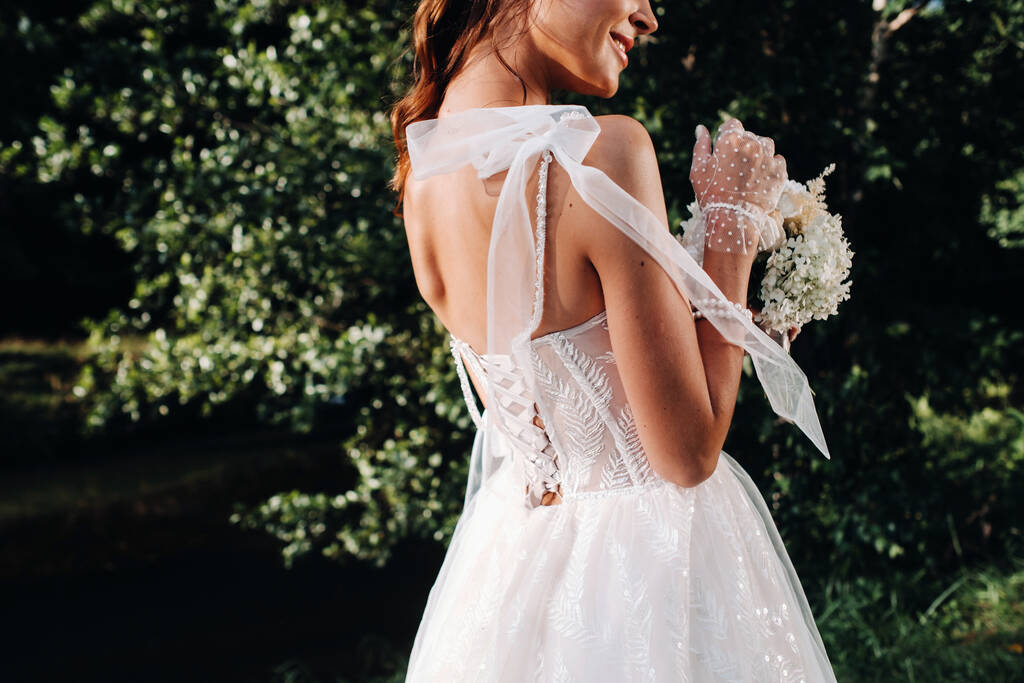 Porträt einer eleganten Braut in einem weißen Kleid mit einem Strauß in der Natur in einem Naturpark. Modell in einem Brautkleid und Handschuhen und mit einem Strauß. Weißrussland. - Foto, Bild