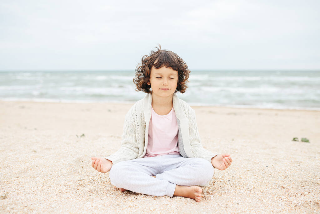 bambina meditando sulla spiaggia, facendo yoga, colori pastello - Foto, immagini