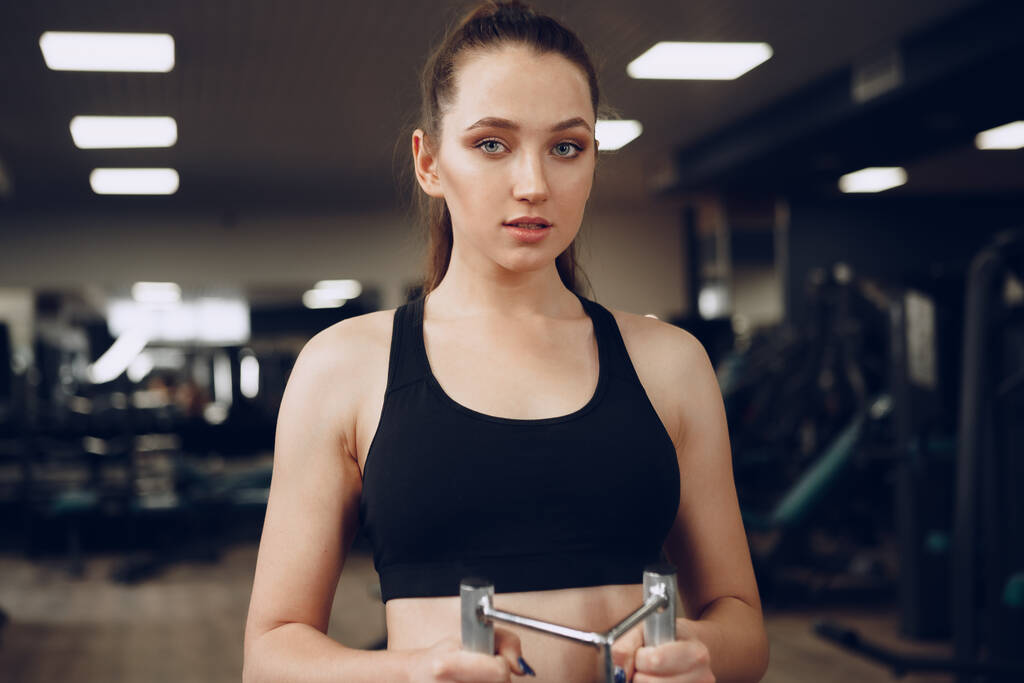 Mujer joven atractiva haciendo ejercicios para los músculos de los brazos y la espalda en un gimnasio - Foto, imagen