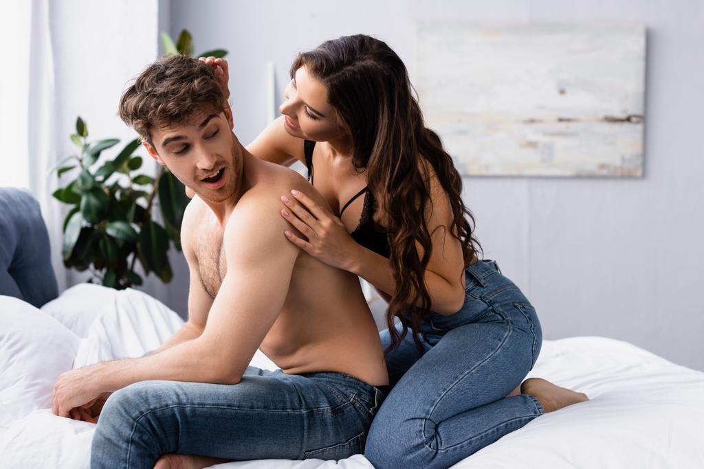 Frau in Jeans sitzt auf Bett neben muskulösem Freund  - Foto, Bild