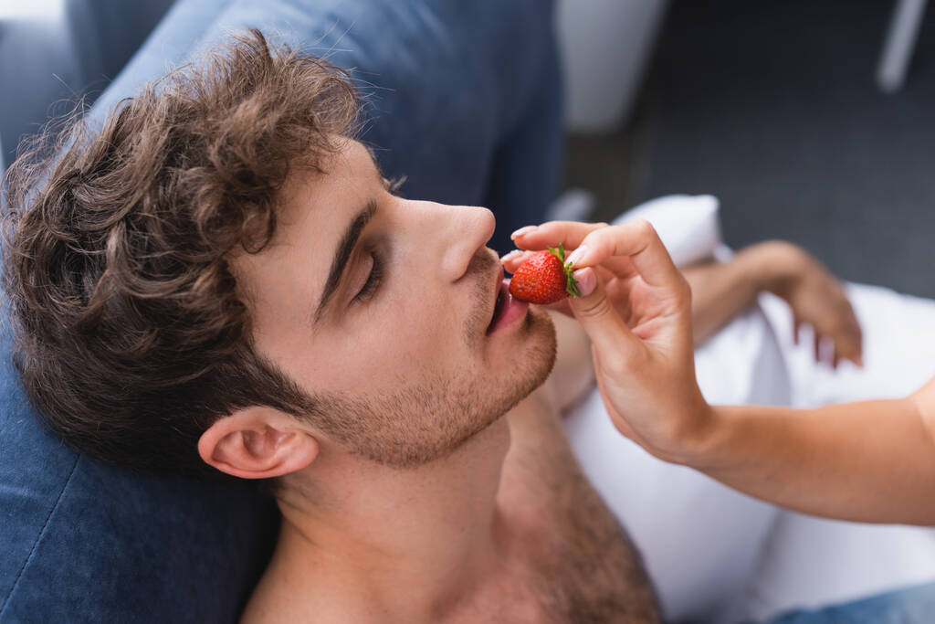 jovem mulher segurando morango e alimentando o homem muscular
 - Foto, Imagem