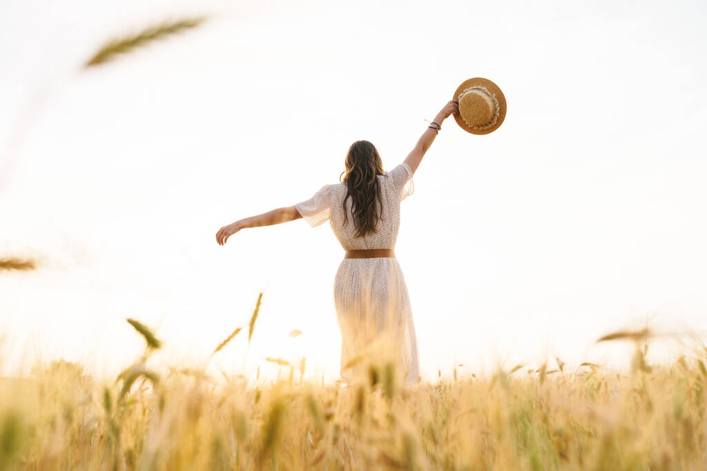Foto de volta da mulher morena bonito com chapéu de palha dançando no campo de trigo no dia de verão
 - Foto, Imagem