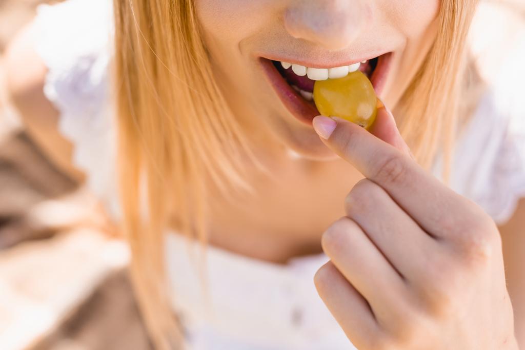 частичный взгляд на молодую женщину, которая ест спелый виноград, избирательный фокус - Фото, изображение