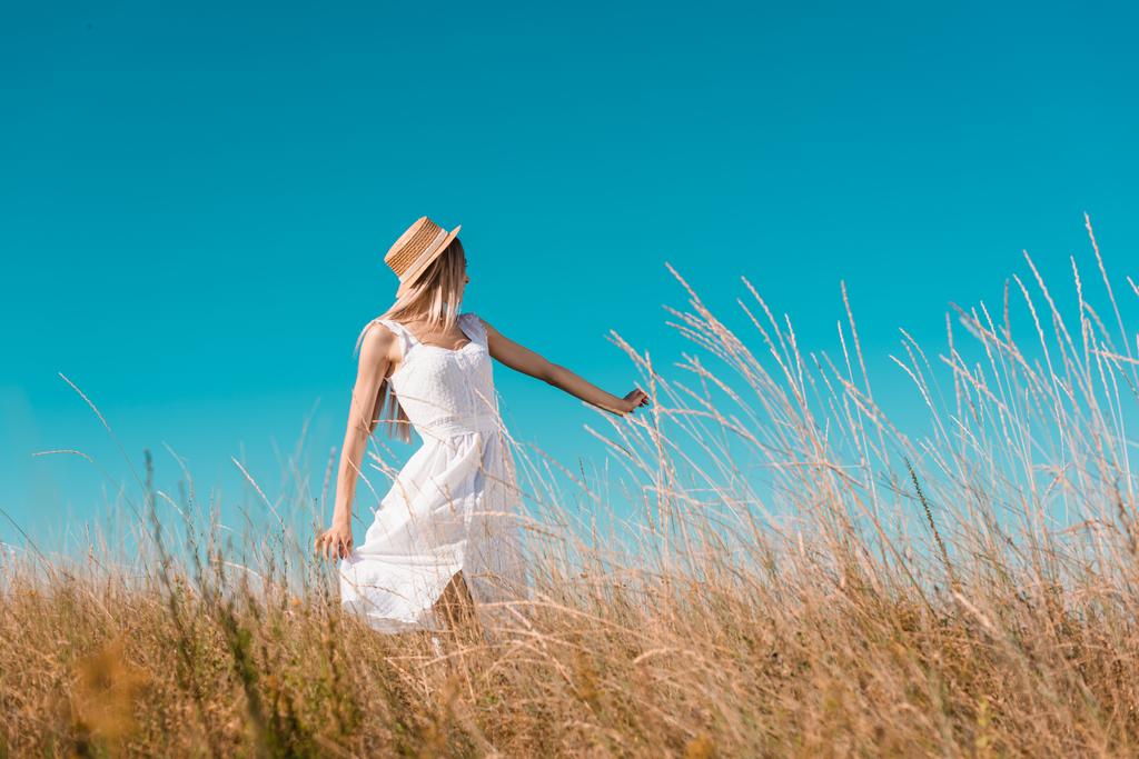 enfoque selectivo de la mujer rubia en vestido blanco y sombrero de paja que muestra sígueme gesto en prado herboso - Foto, imagen