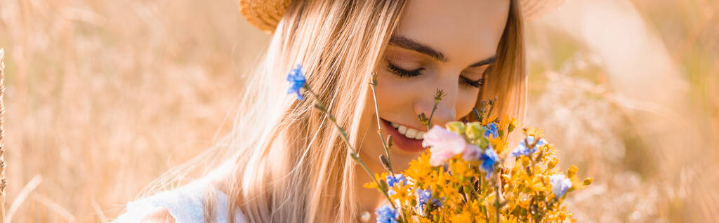 selective focus of sensual woman in straw hat smelling bouquet of wildflowers in field, horizontal concept - Photo, Image