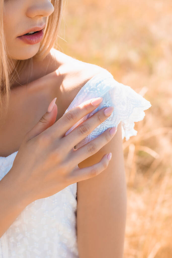 Ausgeschnittene Ansicht einer sinnlichen jungen Frau im Sommeroutfit, die bei Sonnenschein die Schulter berührt - Foto, Bild