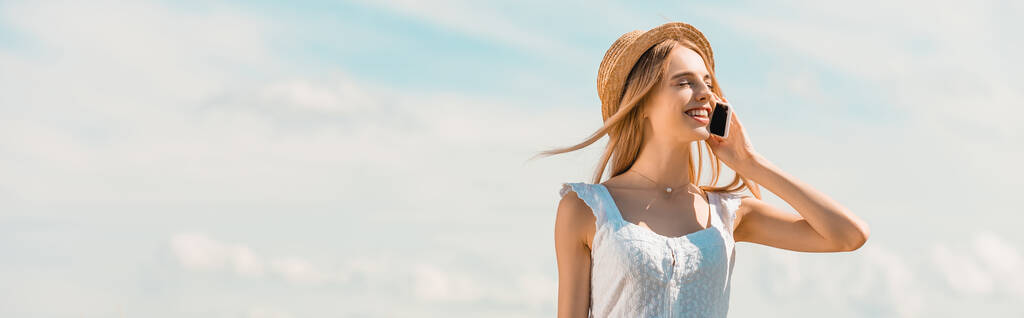 panoramiczne ujęcie blondynki w słomkowym kapeluszu rozmawiającej na smartfonie z zamkniętymi oczami o błękitne niebo - Zdjęcie, obraz