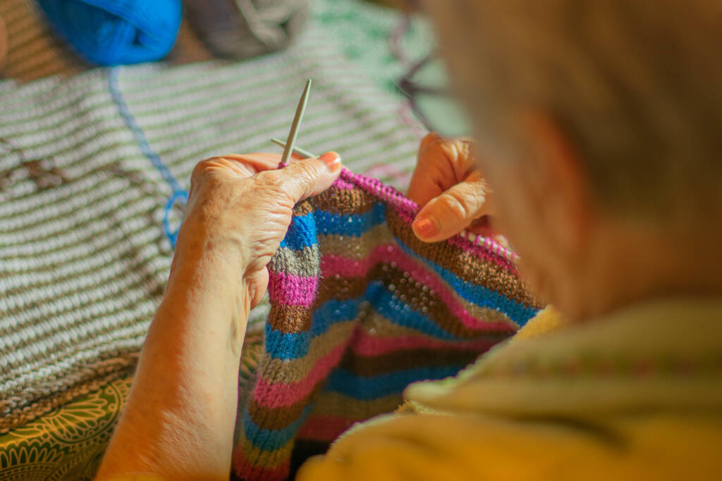Um tiro de perto de uma avó tricotando uma camisola de fios de fio coloridos
 - Foto, Imagem