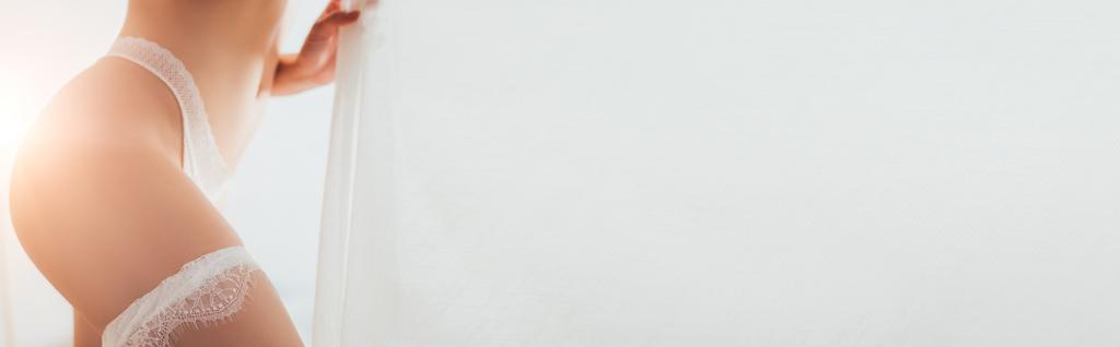 Horizontální plodina nevěsty v kalhotkách a krajkové podvazky dotýkající se záclon  - Fotografie, Obrázek