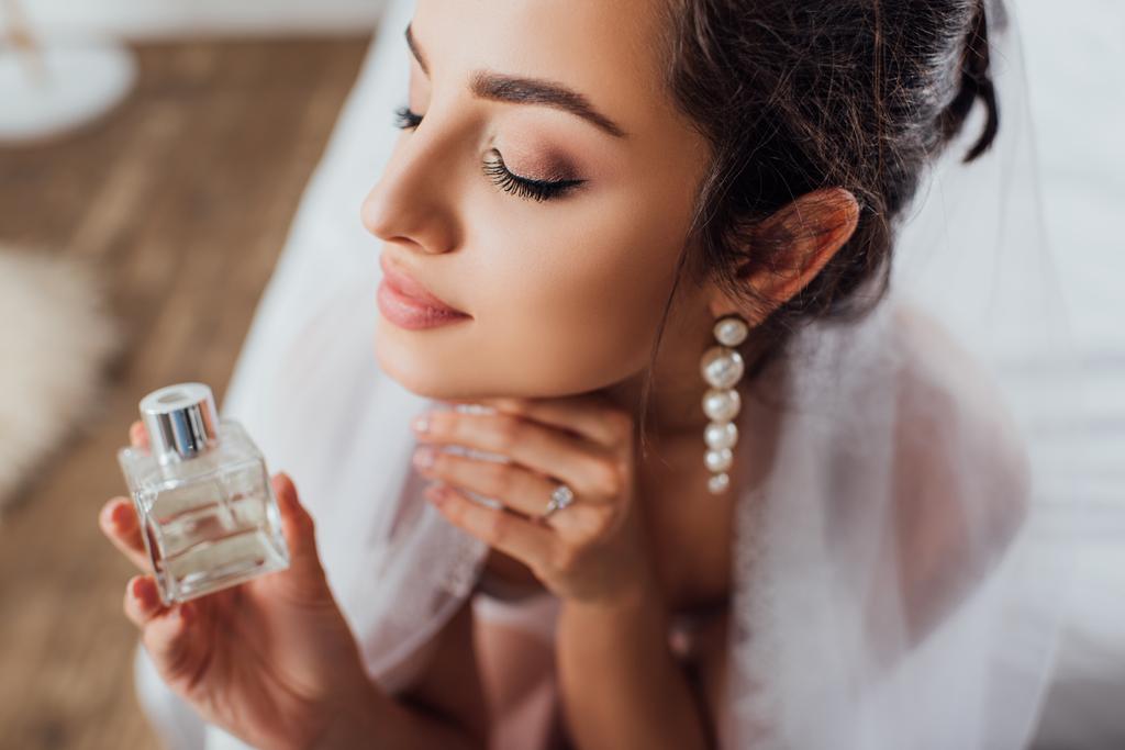 Selectieve focus van jonge bruid in sluier met fles parfum thuis  - Foto, afbeelding