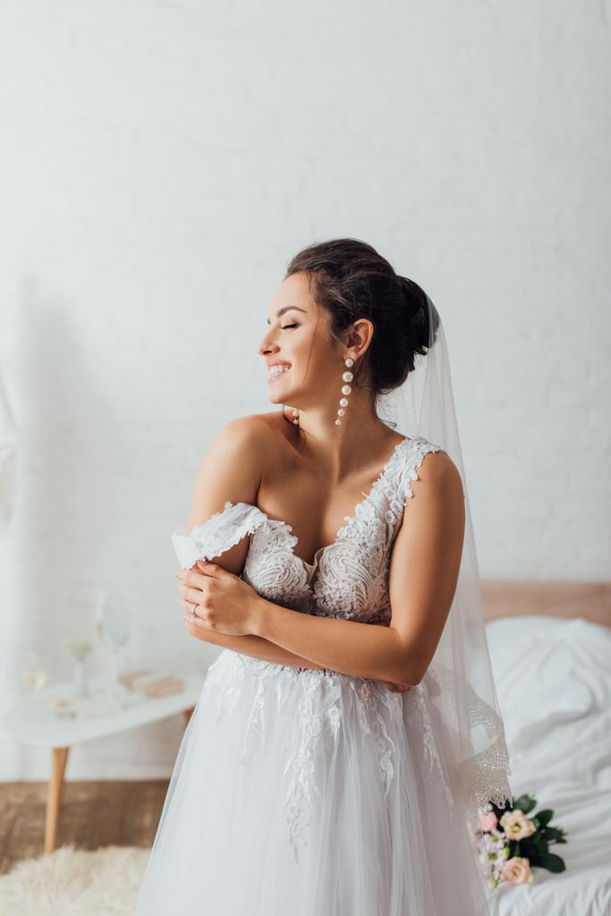 Νεαρή νύφη σε πέπλο με κλειστά μάτια φορώντας νυφικό στην κρεβατοκάμαρα  - Φωτογραφία, εικόνα