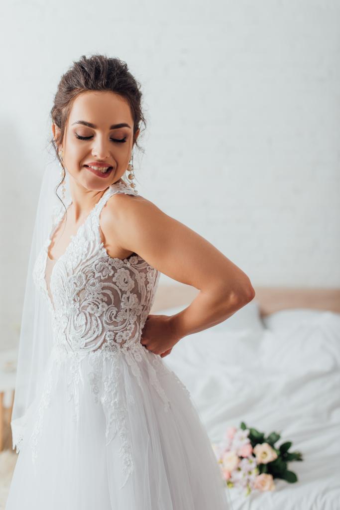 Fiatal menyasszony fátyolban esküvői ruhát vesz fel otthon.  - Fotó, kép