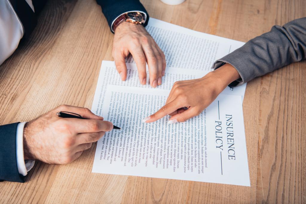 gedeeltelijke weergave van een advocaat die met de vinger wijst naar een verzekeringscontract bij een zakenman met pen - Foto, afbeelding