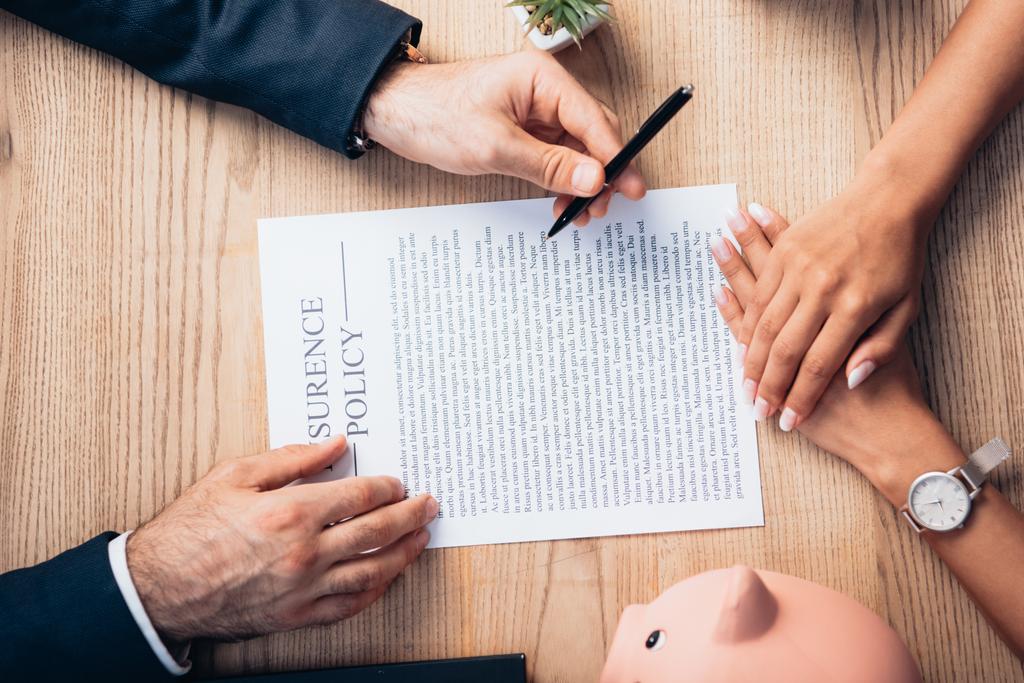 Draufsicht des Rechtsanwalts mit Stift in der Nähe von Versicherungsvertrag, Sparschwein, Pflanze und Frau  - Foto, Bild