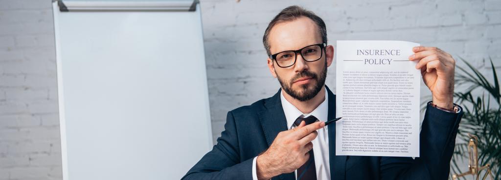 horizontale Ernte von Rechtsanwalt in Brille und Anzug hält Stift und Vertrag mit Versicherungsprotokoll im Büro - Foto, Bild