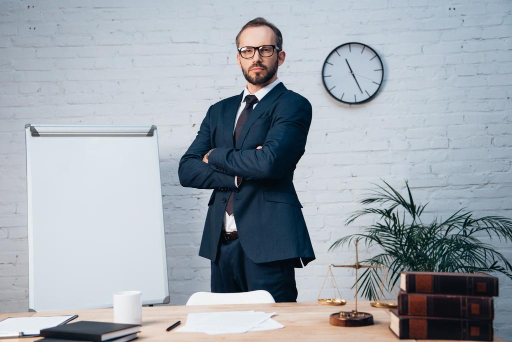 bearded lawyer in glasses standing with crossed arms near table in office - Photo, Image