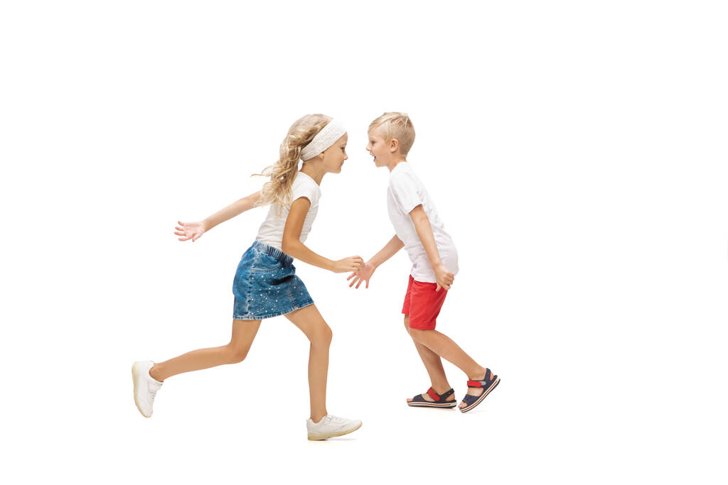 Ευτυχισμένο μικρό καυκάσιο κορίτσι και αγόρι πηδούν και τρέχουν απομονωμένοι σε λευκό φόντο - Φωτογραφία, εικόνα