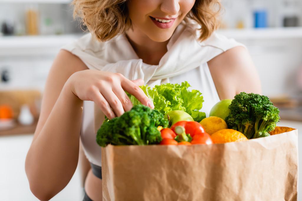 oříznutý pohled mladé ženy dotýkající se potravin v papírové tašce - Fotografie, Obrázek