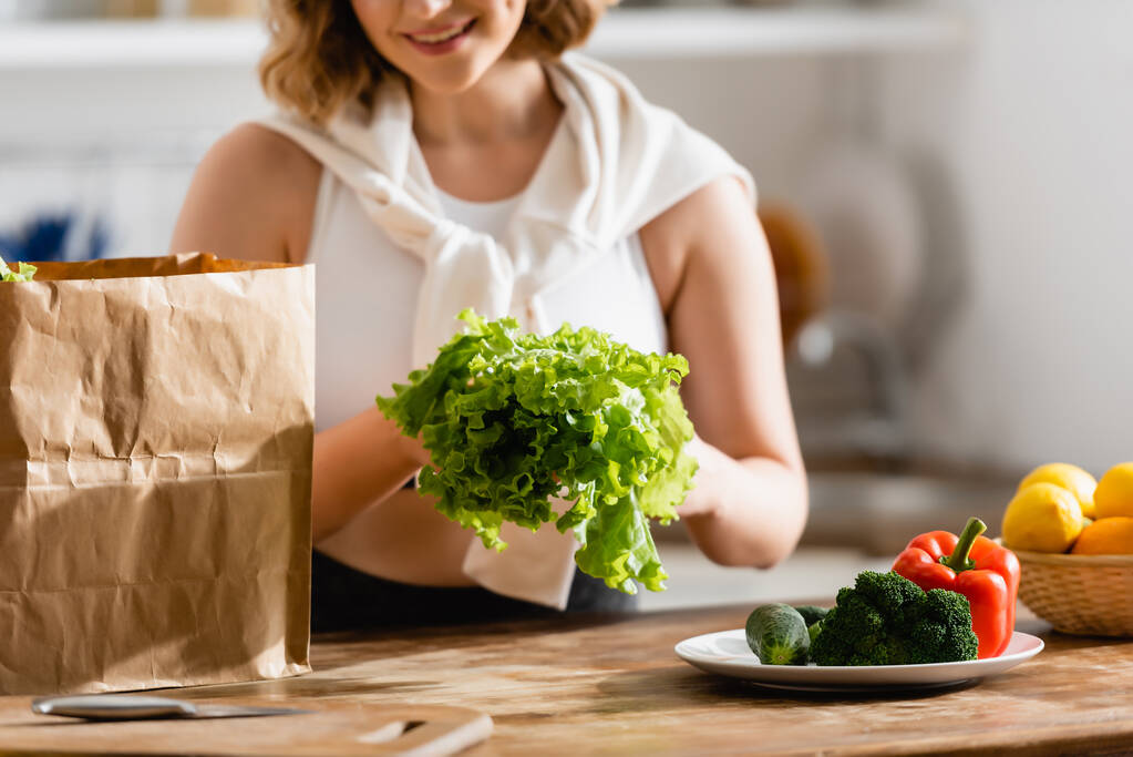 vue recadrée d'une femme tenant de la laitue près de légumes sur une assiette  - Photo, image