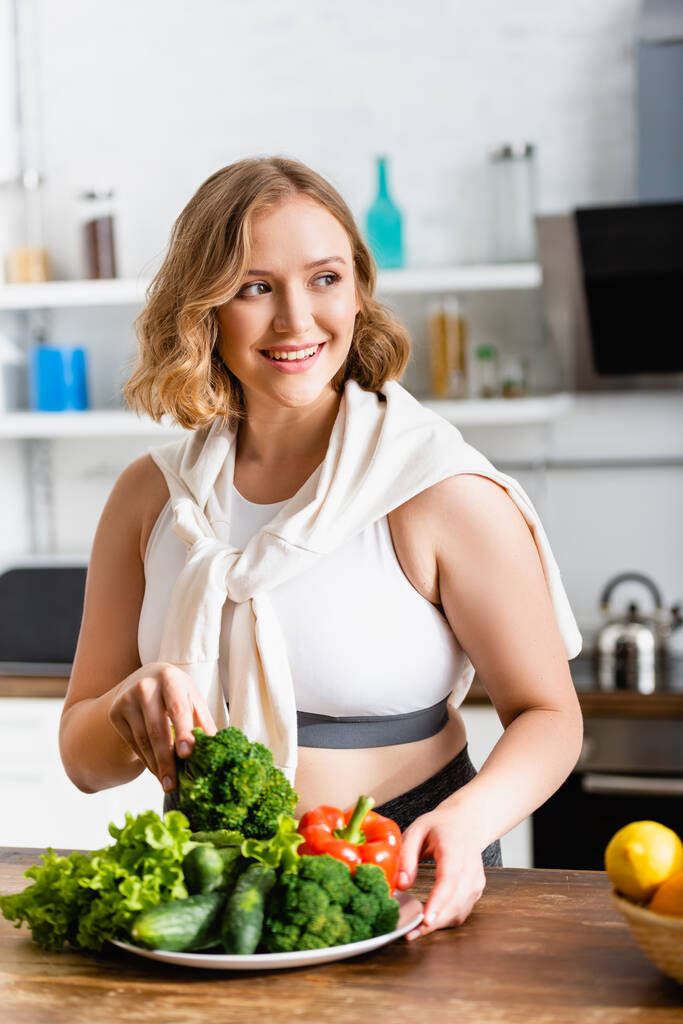 mujer sosteniendo brócoli fresco cerca de verduras maduras en el plato - Foto, Imagen
