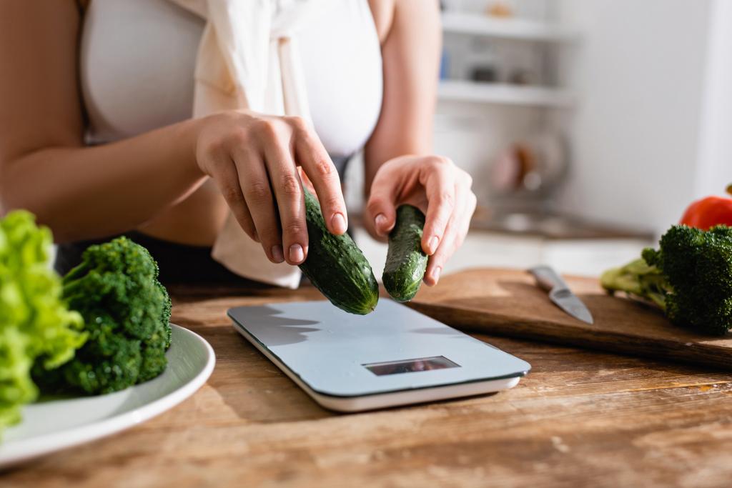 cropped view of woman putting cucumbers on kitchen scales - Photo, Image