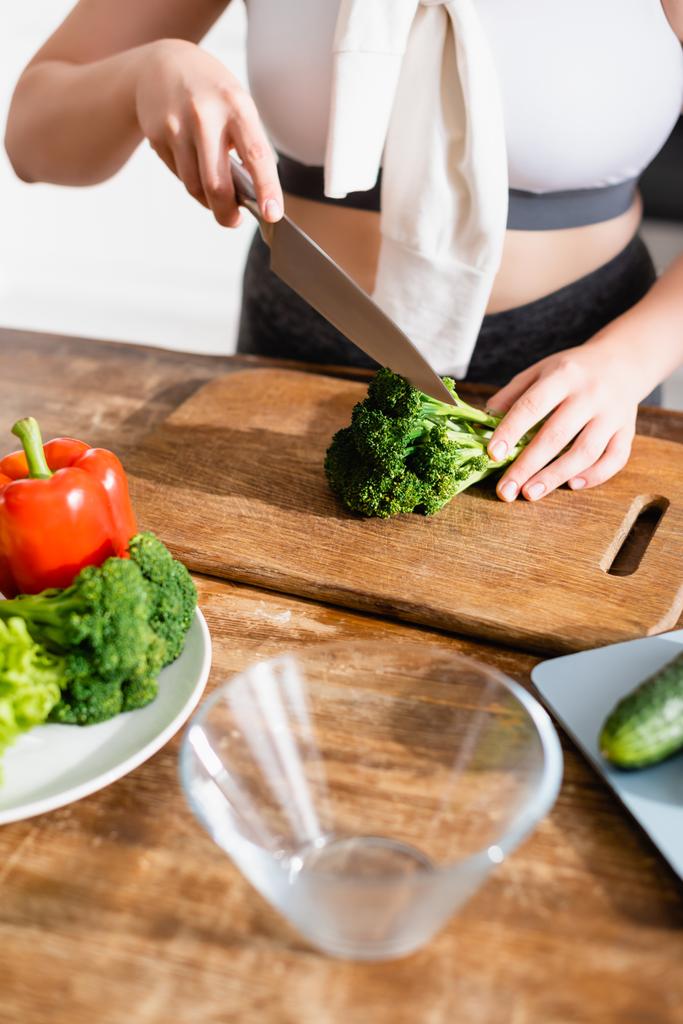 vista ritagliata di donna che taglia broccoli freschi sul tagliere vicino alle verdure  - Foto, immagini