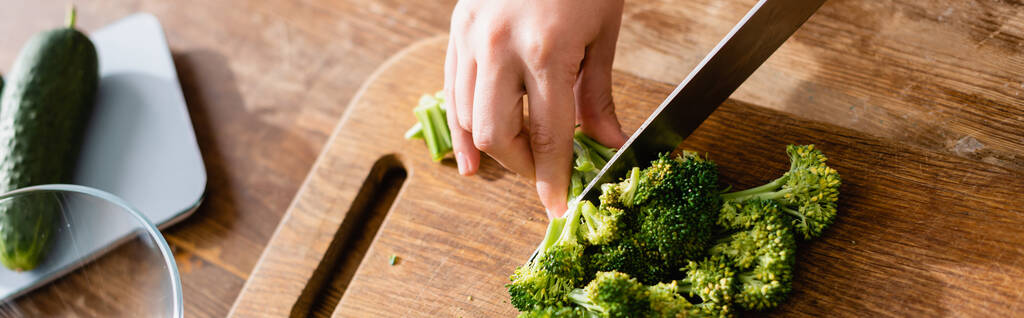 culture panoramique de femme coupant brocoli frais sur planche à découper près des balances de cuisine avec concombre - Photo, image