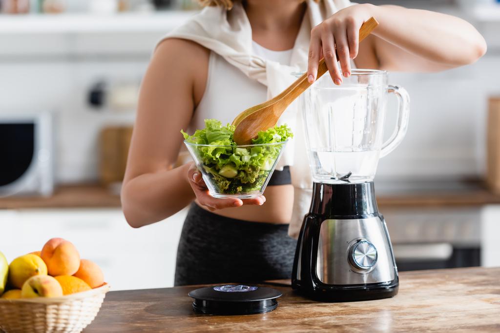 abgeschnittene Ansicht einer Frau mit Schüssel mit Salat und Kochlöffel in der Nähe des Mixers  - Foto, Bild