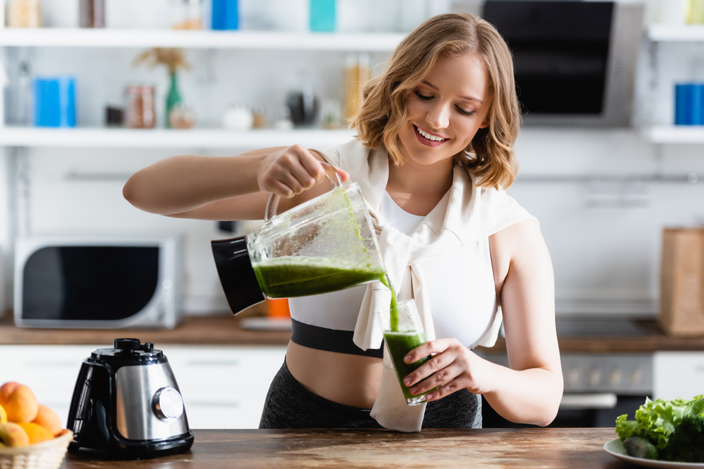 selective focus of young woman pouring green smoothie in glass near fruits - Photo, Image