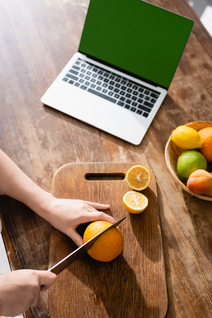 cropped view of woman cutting lemon near laptop with green screen - Photo, Image